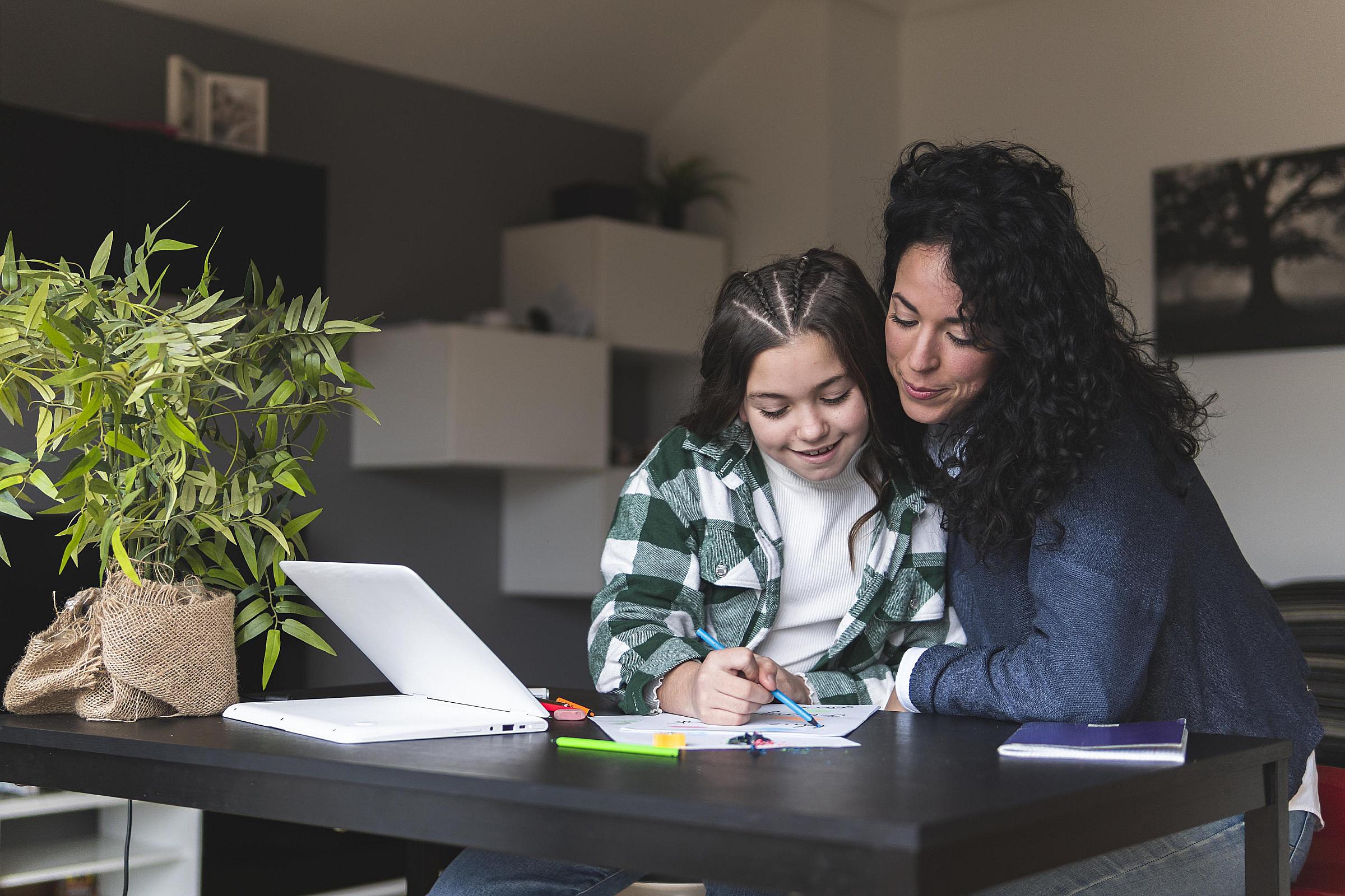 Mother sitting with child at desk helping with school work